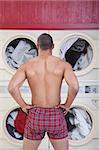 Muscular man in boxer shorts waits in front of washing machines