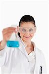 Dark-haired scientist with safety glasses holding a blue flask in front of the camera