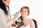 Cute blond-haired woman having her make up done by a make up artist in a studio