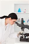 Dark-haired female scientist looking through a microscope in a lab