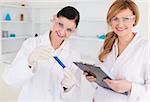 Two scientists looking at the camera while holding a test tube and a notapad in a lab