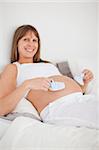 Charming pregnant woman playing with little socks while lying on a bed in her apartment