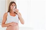 Cute pregnant female taking a pill while sitting on a bed in her apartment