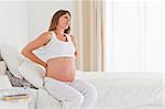 Attractive pregnant female having a back pain while sitting on a bed in her apartment