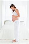 Attractive pregnant female using a scale while standing in her bedroom