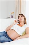 Portrait of a happy pregnant woman phoning in her living room