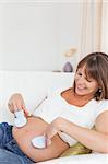 Pregnant woman playing with baby shoes while lying in her living room