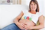 Pretty pregnant woman playing with wooden blocks while lying on a sofa in her living room