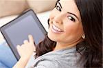 Beautiful happy young Latina Hispanic woman smiling and using a tablet computer or iPad at home on her sofa