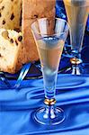 Panettone the italian Christmas fruit cake served on a blue glass plate over a blue fabric background and two glasses of spumante (sparkling wine). Selective focus.