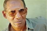 portrait of mature hispanic man with sunglasses looking at camera against green wall with serious expression. Copy space