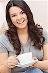 A beautiful young Latina Hispanic woman or girl with a wonderful enigmatic smile drinking tea or coffee from a white cup