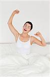 Portrait of a charming woman stretching her arms in her bedroom