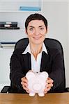 Portrait of a smilling office worker holding a piggybank in her office