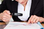 Femine hands holding a magnifying glass above a chart in a office