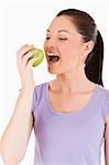 Beautiful woman eating an apple while standing against a white background