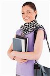 Charming student holding books and her bag while standing against a white background