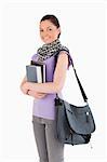 Beautiful student holding books and her bag while standing against a white background