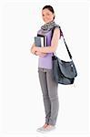 Attractive student holding books and her bag while standing against a white background