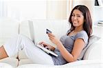 young woman smiling into camera with credit card in hands in livingroom