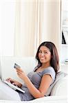 cute woman sitting on sofa in livingroom holding credit card smiles into camera