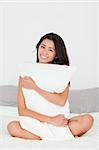 smiling woman with pillow sitting on her bed looking into camera in bedroom