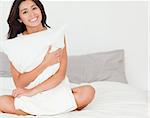 charming woman with pillow sitting on her bed looking into camera in bedroom