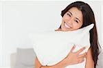 close up of a charming woman with pillow sitting on her bed looking into camera in bedroom