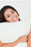 close up of a cute woman with pillow sitting on her bed looking into camera in bedroom