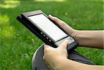 Young woman reads electronic book sitting on the grass.