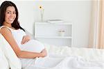 Good looking pregnant woman touching her belly while lying on a bed at home