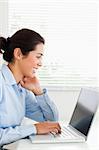Charming woman working with her laptop and typing while sitting at the office