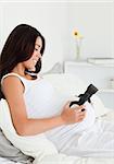 Charming pregnant woman putting headphones on her belly while lying on a bed at home