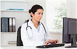 Gorgeous female doctor typing on a keyboard while sitting in her office