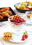 White yogurt with caramelized berries with chicken wings and vegetable salad in background