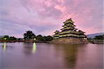 The historic Matsumoto Castle under pink skies, dating from the 15th Century in Matsumoto, Japan.