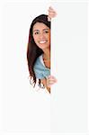 Good looking woman hiding behind a board while standing against a white background