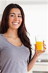 Beautiful woman holding a glass of orange juice while standing in the kitchen