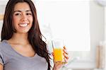 Good looking woman holding a glass of orange juice while standing in the kitchen