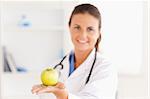 Doctor with stethoscope holding an apple looking at the camera in the surgery