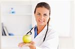 Doctor with stethoscope holding an apple looking into the camera in the surgery