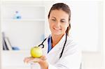 Smiling doctor with stethoscope holding an apple in the surgery