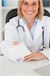 Smiling blonde doctor giving prescription looks into camera in her office