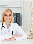 Smiling doctor with model spine next to her looks into camera in her office