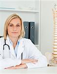 Serious doctor with model spine next to her looks into camera in her office