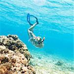 Beautiful woman diver swimming among the coral reef