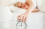 Upset woman switching off her alarm clock in her bedroom
