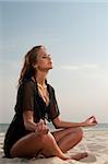 young woman sitting in lotus position on a beach
