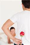 Handsome guy hiding a rose from his girlfriend in the bedroom