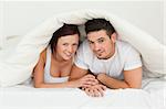 Cherrful couple hiding under a blanket in the bedroom